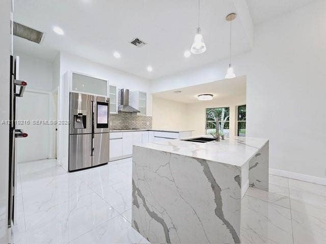 Kitchen featuring a waterfall-edge island with stone-finish countertops, stainless steel appliances, white cabinetry with glass-panel uppers, tile backsplash, and large-format porcelain tile flooring