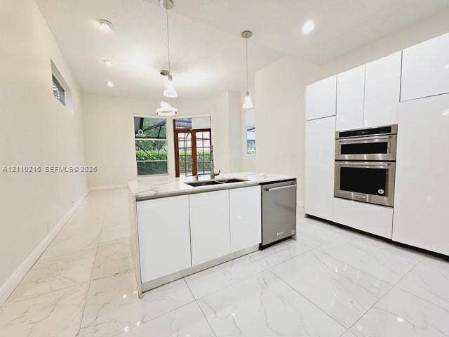 Modern kitchen featuring floor-to-ceiling white cabinetry, stone-finish countertops, stainless steel double wall ovens, a central island with an integrated sink, and large-format porcelain tile flooring