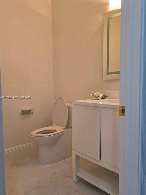 Bathroom featuring stone-finish floor tile, white vanity with integrated basin, back-lit wall mirror, and modern toilet