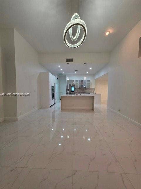 Large-format porcelain tile flooring with veining detail, central island with waterfall edge, recessed ceiling lighting, and sculptural multi-ring pendant fixture