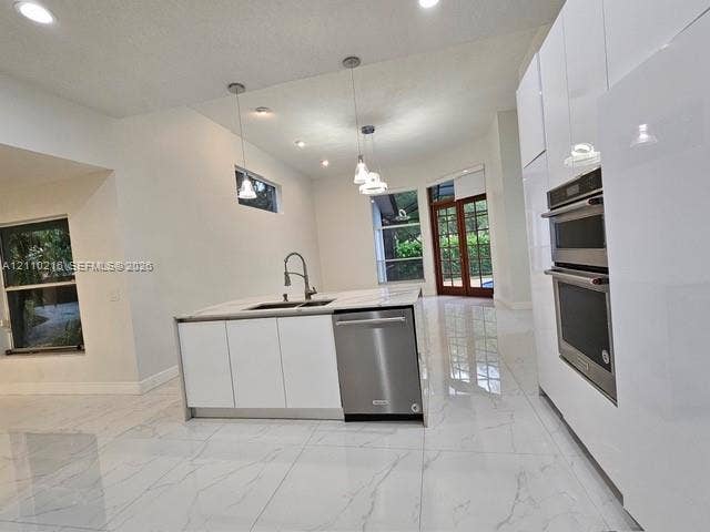 Modern kitchen featuring high-gloss white cabinetry, a center island with a stone-finish countertop, stainless steel double wall ovens, a stainless steel dishwasher, and polished tile flooring