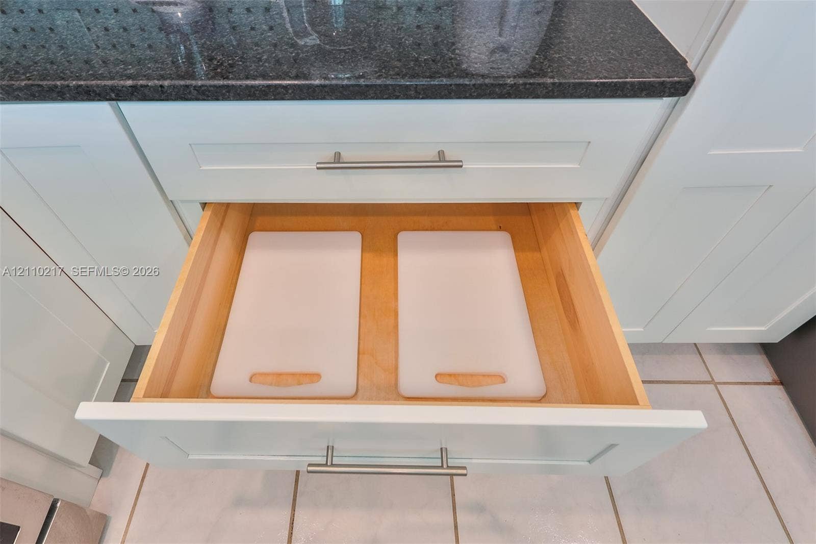 503 SW 17 Street, Cape Coral, FL 33990 Shaker-style white cabinetry featuring a pull-out drawer with a light-finish wood interior, brushed-metal hardware, and dark stone-finish countertop