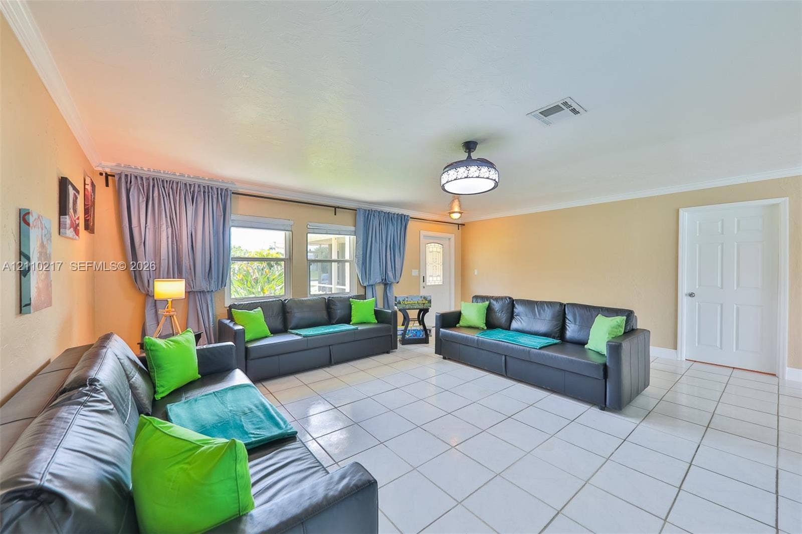 503 SW 17 Street, Cape Coral, FL 33990 Living area featuring large format white tile flooring, crown molding, double windows with wall-mounted curtain hardware, and a ceiling fan with integrated lighting