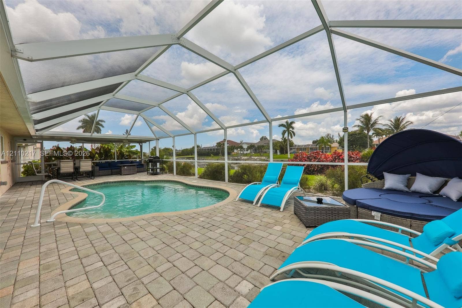 503 SW 17 Street, Cape Coral, FL 33990 Screened-in patio featuring a concrete paver deck, a kidney-shaped pool, and an integrated handrail