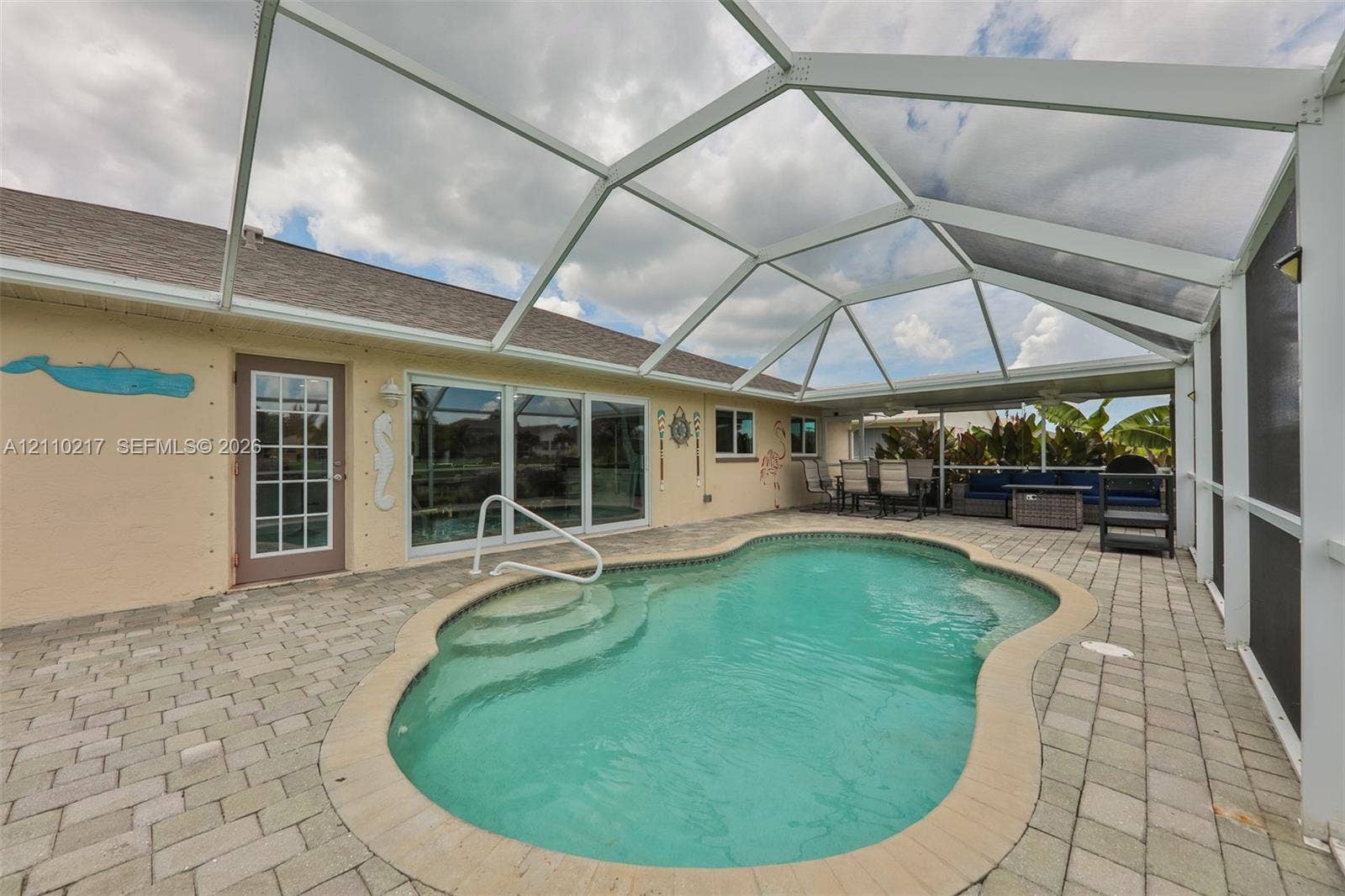 503 SW 17 Street, Cape Coral, FL 33990 Screen-enclosed patio featuring a paver deck and a custom-shaped swimming pool with built-in steps and a metal handrail