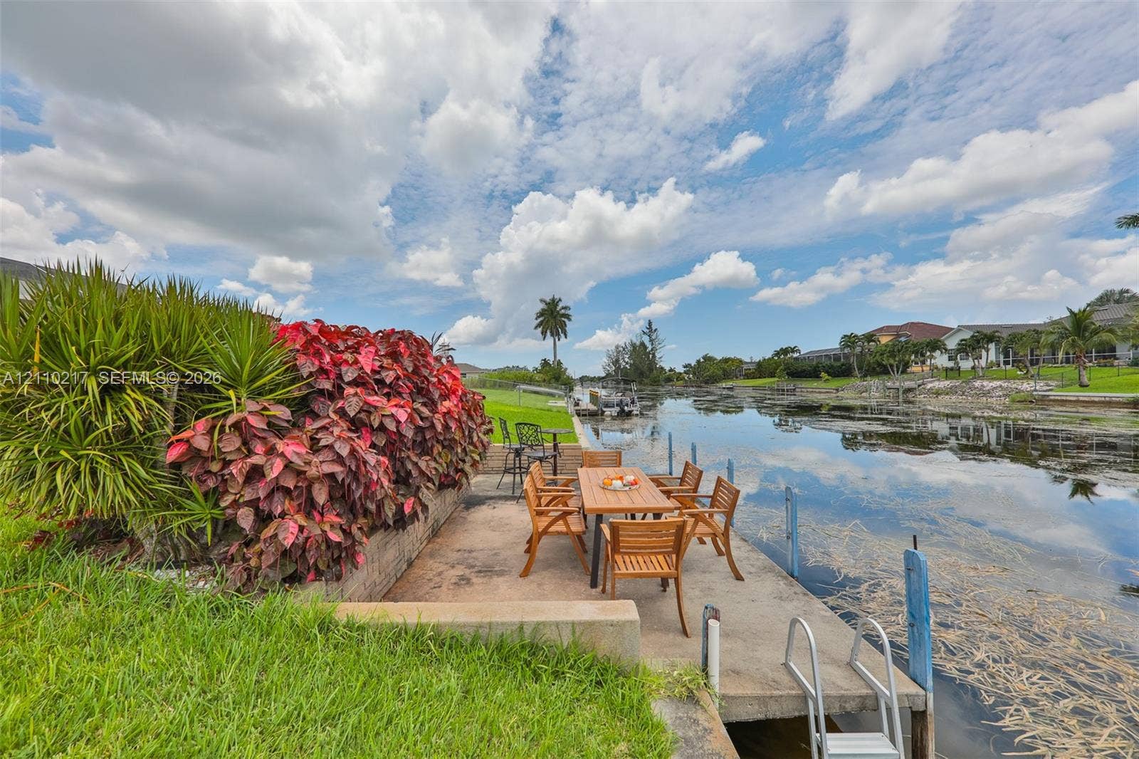 503 SW 17 Street, Cape Coral, FL 33990 Waterfront concrete dock featuring a built-in swimming ladder, stone retaining wall, and mature tropical landscaping
