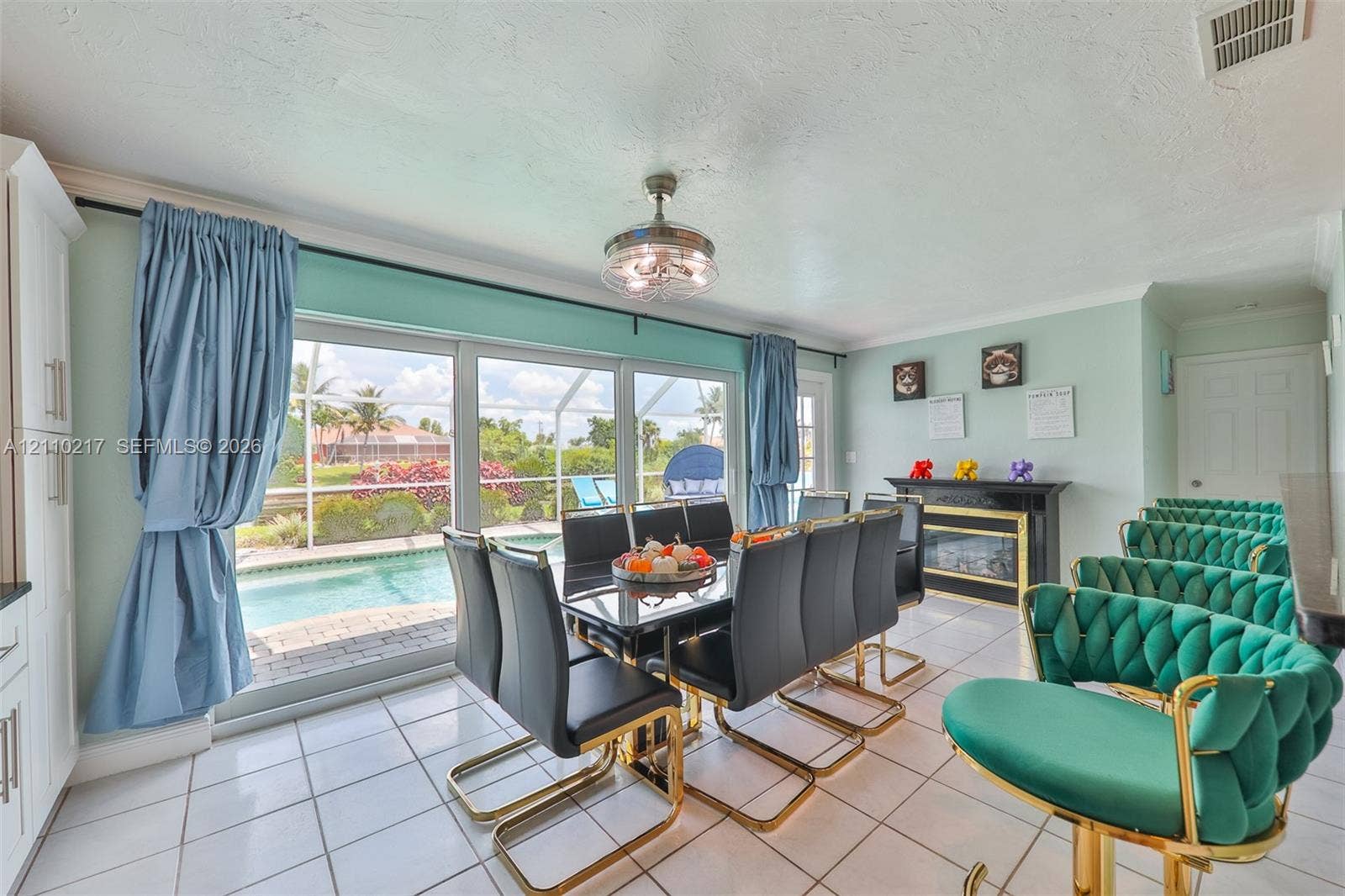 503 SW 17 Street, Cape Coral, FL 33990 Open-concept dining area featuring large sliding glass doors, white ceramic tile flooring, a mounted electric fireplace with a black surround, and a central ceiling fan with integrated lighting
