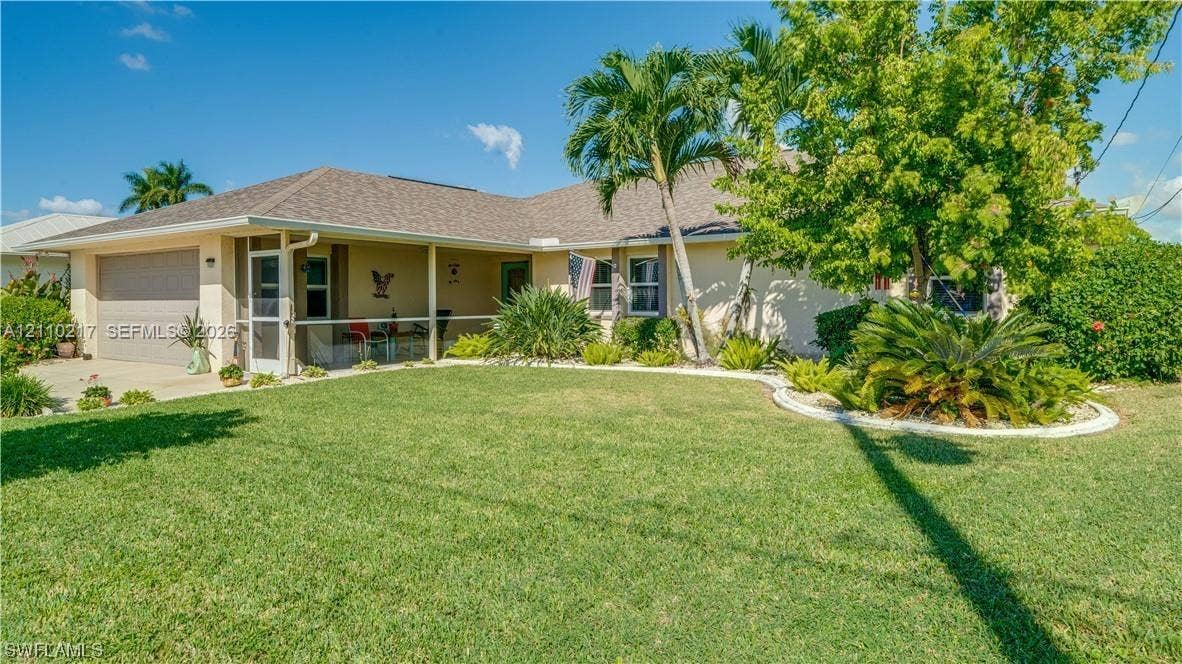 503 SW 17 Street, Cape Coral, FL 33990 Single-story residence featuring a covered front entryway, attached two-car garage, and asphalt shingle roofing, complemented by established palm trees and manicured landscape curbing
