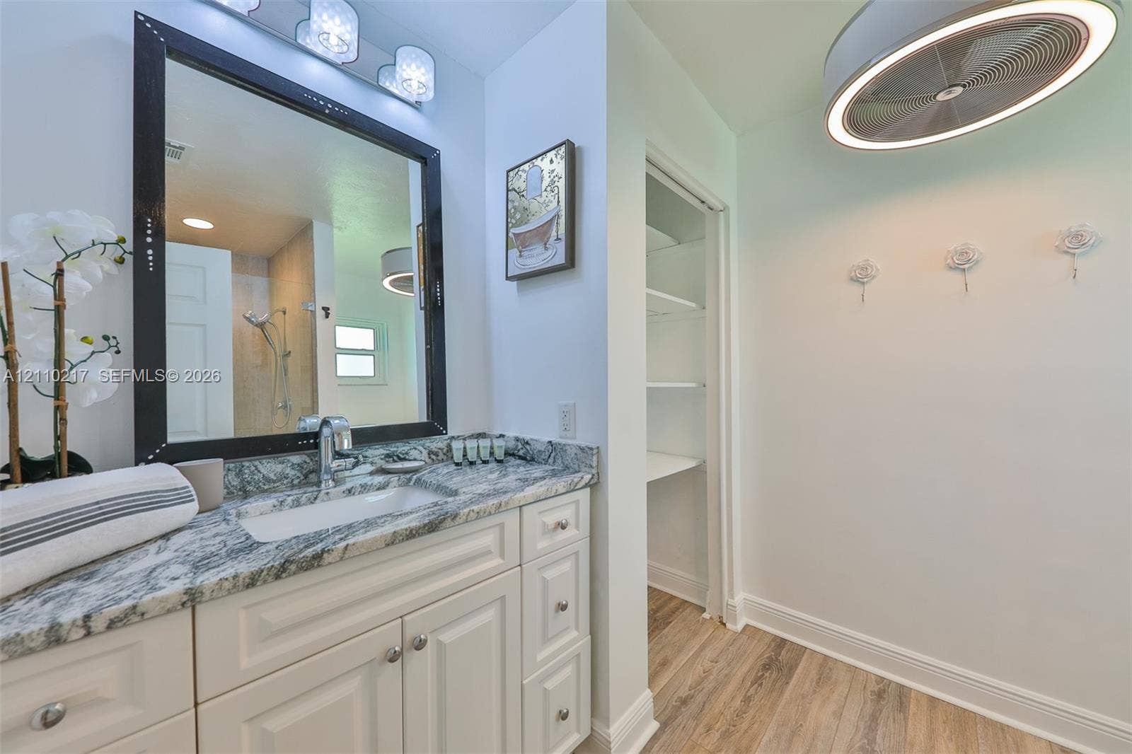 503 SW 17 Street, Cape Coral, FL 33990 Vanity featuring stone-finish countertop with undermount sink, framed mirror, built-in cabinetry, wood-finish flooring, and integrated wall shelving