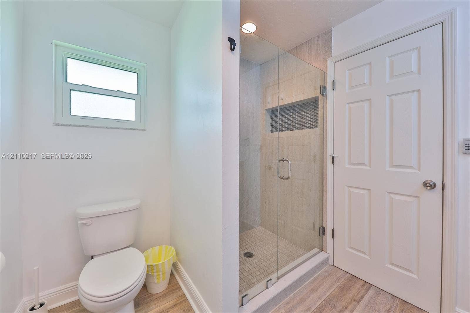 503 SW 17 Street, Cape Coral, FL 33990 Bathroom featuring a glass-enclosed shower with tiled surround and built-in niche, wood-finish flooring, and a six-panel door