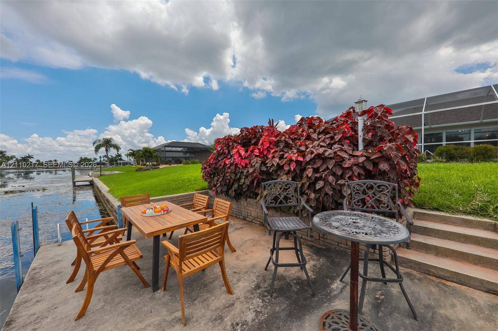 503 SW 17 Street, Cape Coral, FL 33990 Waterfront patio featuring a concrete hardscape, stone retaining wall, and mature landscaping