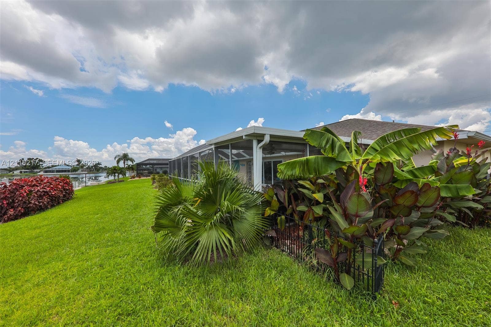 503 SW 17 Street, Cape Coral, FL 33990 Screened-in lanai featuring a manicured lawn, established tropical landscaping, and water frontage