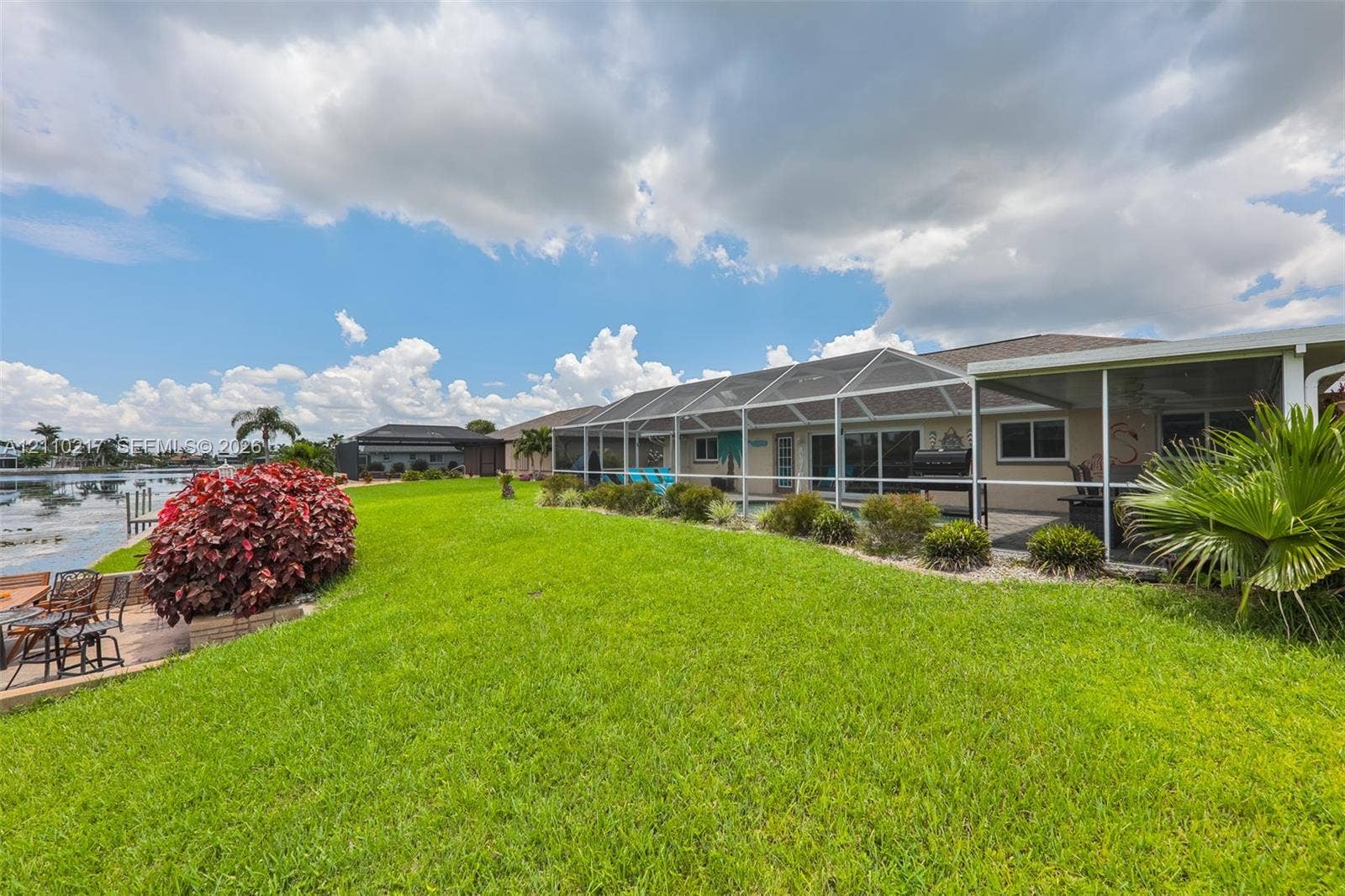 503 SW 17 Street, Cape Coral, FL 33990 Rear exterior featuring a screened-in lanai, manicured lawn, water frontage, and native landscaping