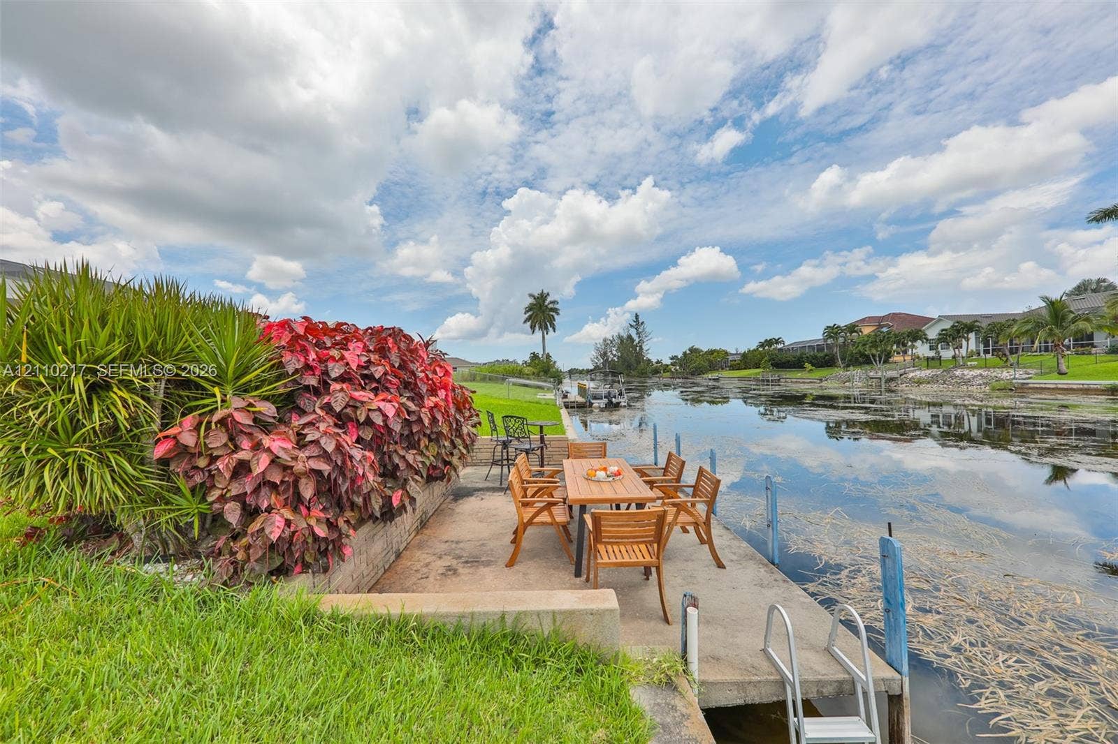 503 SW 17 Street, Cape Coral, FL 33990 Concrete waterfront dock featuring a built-in ladder, canal bulkhead, and integrated landscaping with mature foliage