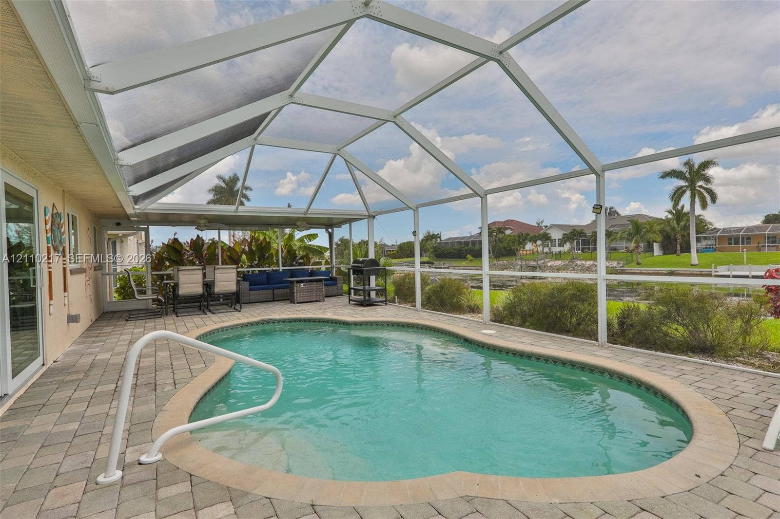 503 SW 17 Street, Cape Coral, FL 33990 Screened-in patio area featuring a paver deck, inground swimming pool with a metal handrail, and a covered lanai