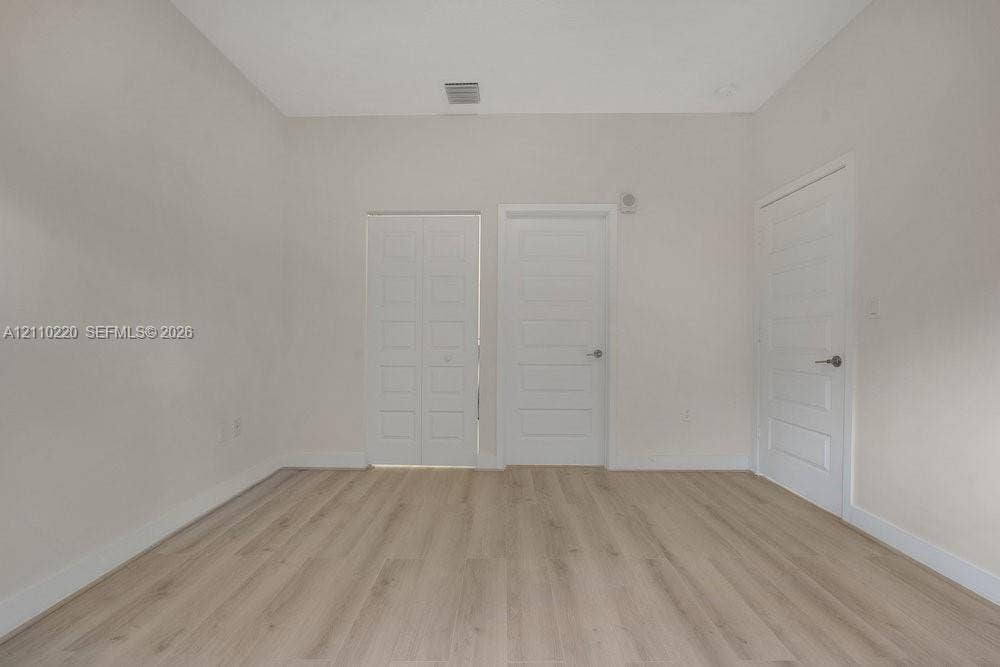 Room featuring light-toned wood-finish flooring, neutral walls, two five-panel interior doors, and one set of bifold closet doors with brushed nickel hardware