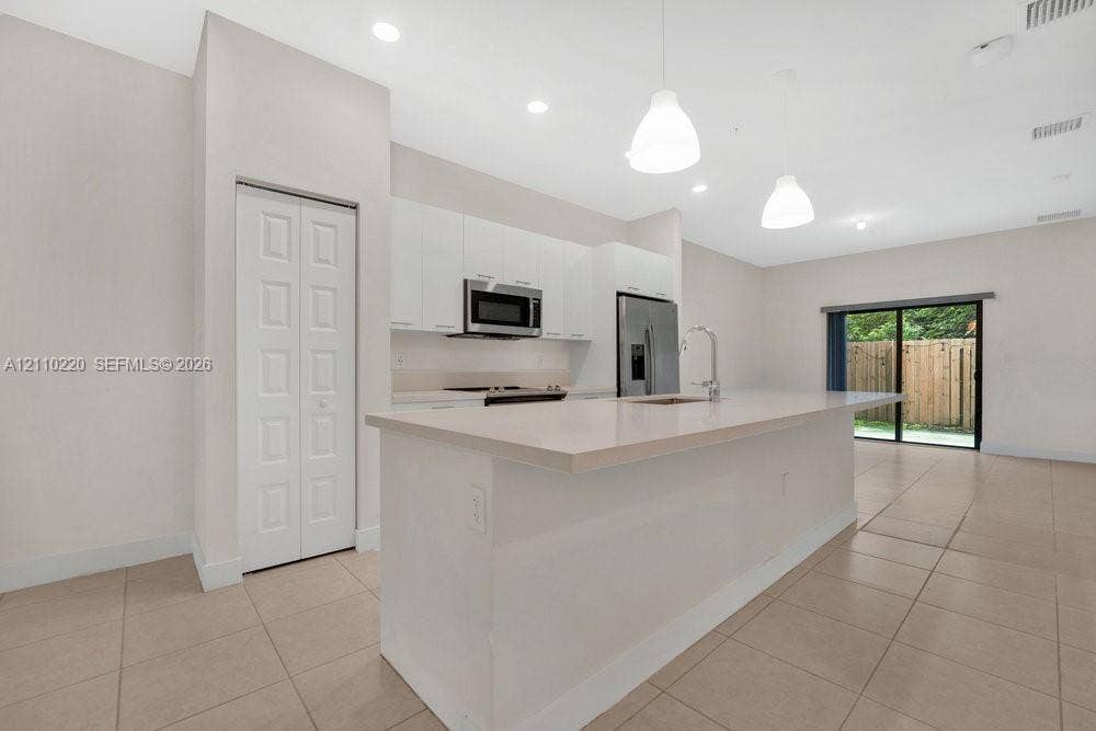 Kitchen featuring flat-panel white cabinetry, a center island with a stone-composite countertop, stainless steel appliances, and tile flooring