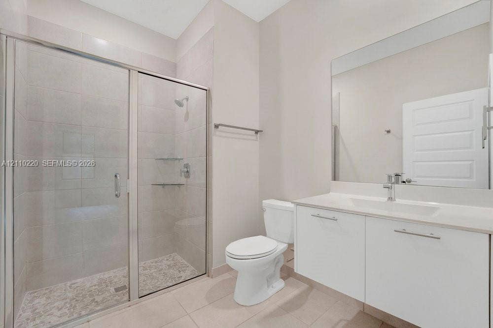Bathroom featuring a glass-enclosed shower with tiled walls and flooring, a wall-to-wall vanity with an integrated sink, a large vanity mirror, and a chrome-finish faucet