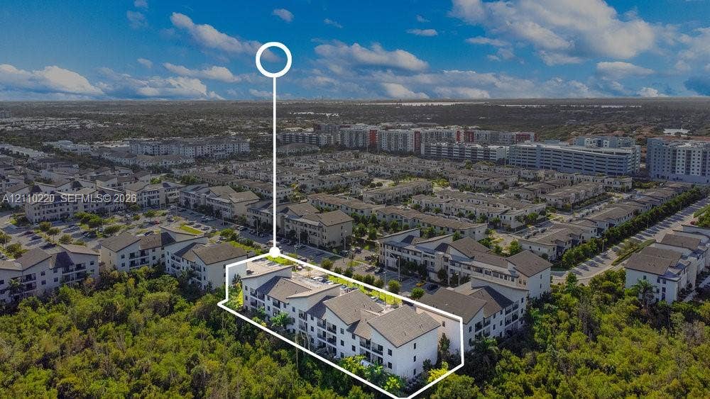 Aerial perspective of a multi-story residential building featuring a light-toned exterior, gabled rooflines, and private balconies, situated along a dense woodland border