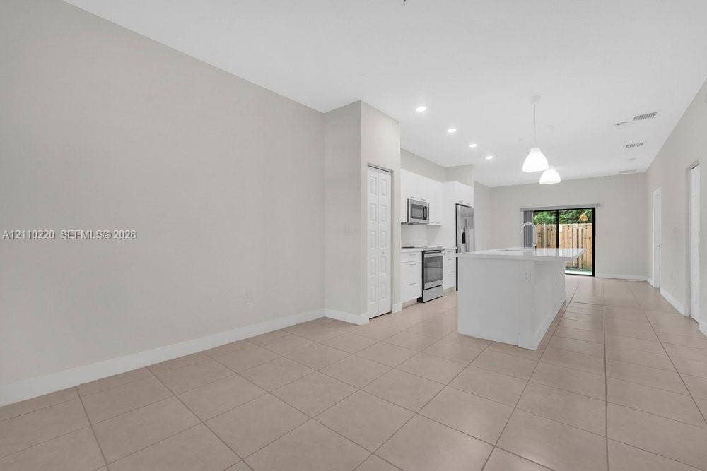 Open-concept kitchen featuring a center island with countertop seating, white cabinetry, stainless steel appliances, tile flooring, and recessed lighting