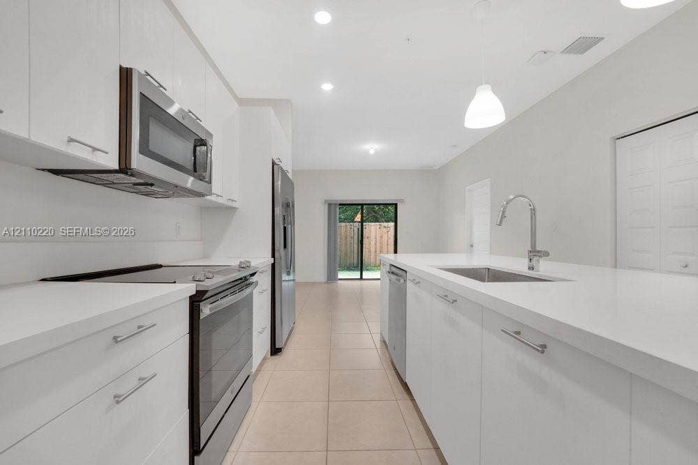 Kitchen featuring white flat-panel cabinetry, solid-surface countertops, a stainless steel undermount sink with a gooseneck faucet, stainless steel appliances, and tile flooring