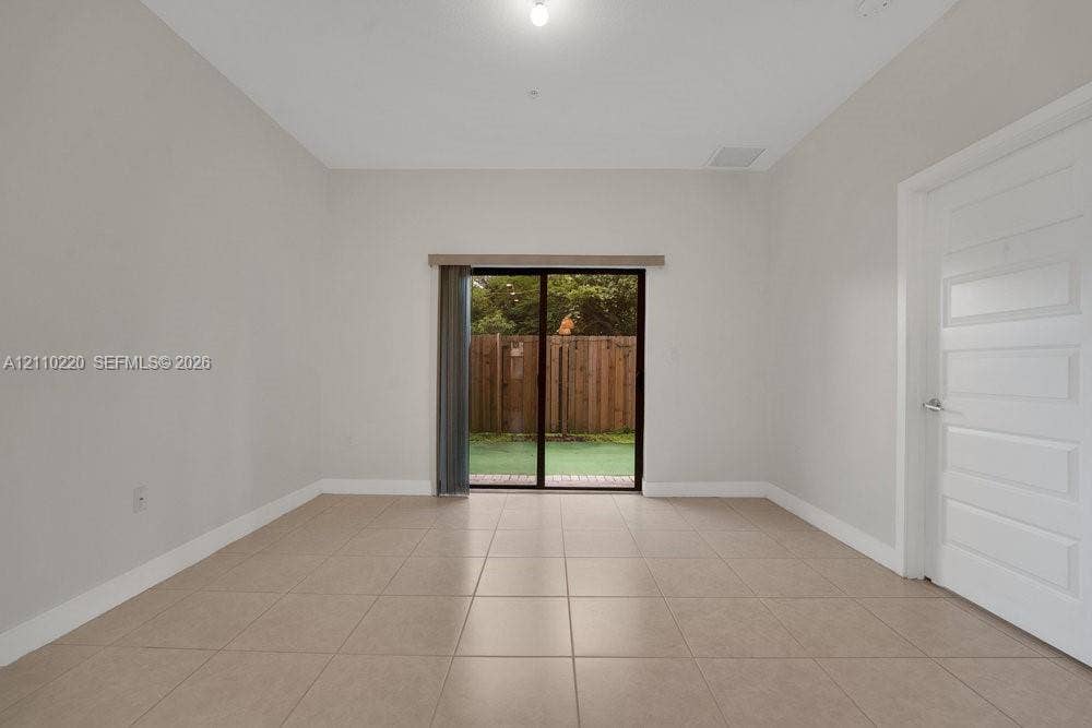 Neutral-toned interior featuring large-format floor tiles, high ceilings, a five-panel interior door, and sliding glass doors with access to an exterior fenced area