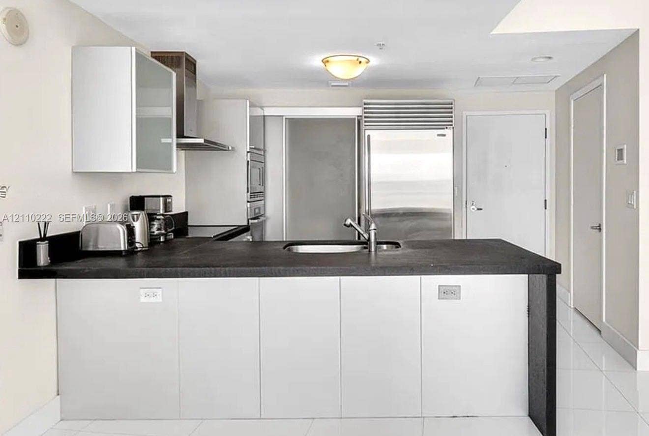 18201 Collins Avenue, #2008, Sunny Isles Beach, Sunny Isles Beach, FL 33160 Kitchen featuring flat-panel cabinetry, a stainless steel refrigerator, stone-surfaced island with an integrated sink, and stainless steel range hood