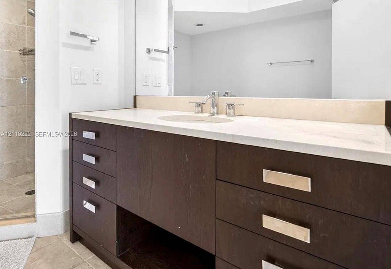 18201 Collins Avenue, #2008, Sunny Isles Beach, Sunny Isles Beach, FL 33160 Bathroom vanity featuring dark wood-finish cabinetry, a neutral solid-surface countertop with an integrated oval sink, polished metal hardware, and a large-format mirror