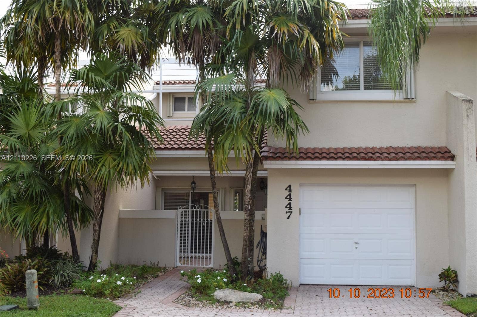 Two-story exterior featuring a tile roof, single-car garage, brick paver driveway, and a gated courtyard entry