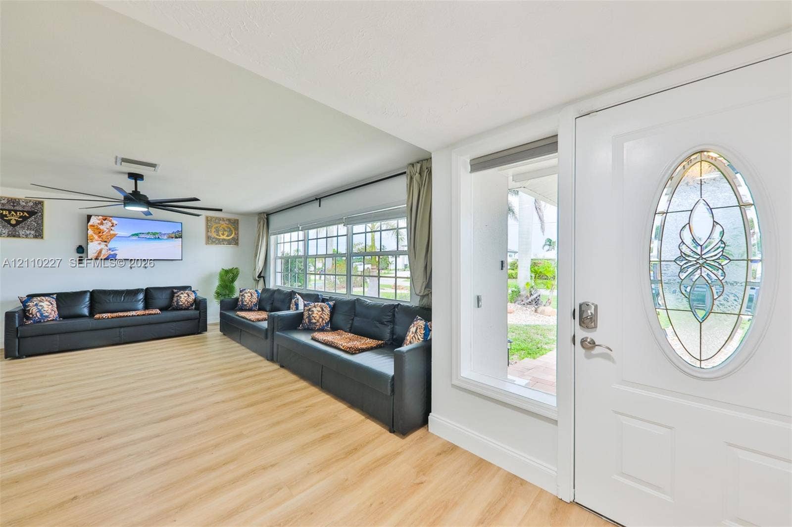 450 Bayshore Drive, Cape Coral, FL 33904 Entrance featuring a white door with an oval decorative glass insert, wood-finish flooring, multi-pane windows, and a black ceiling fan with integrated lighting