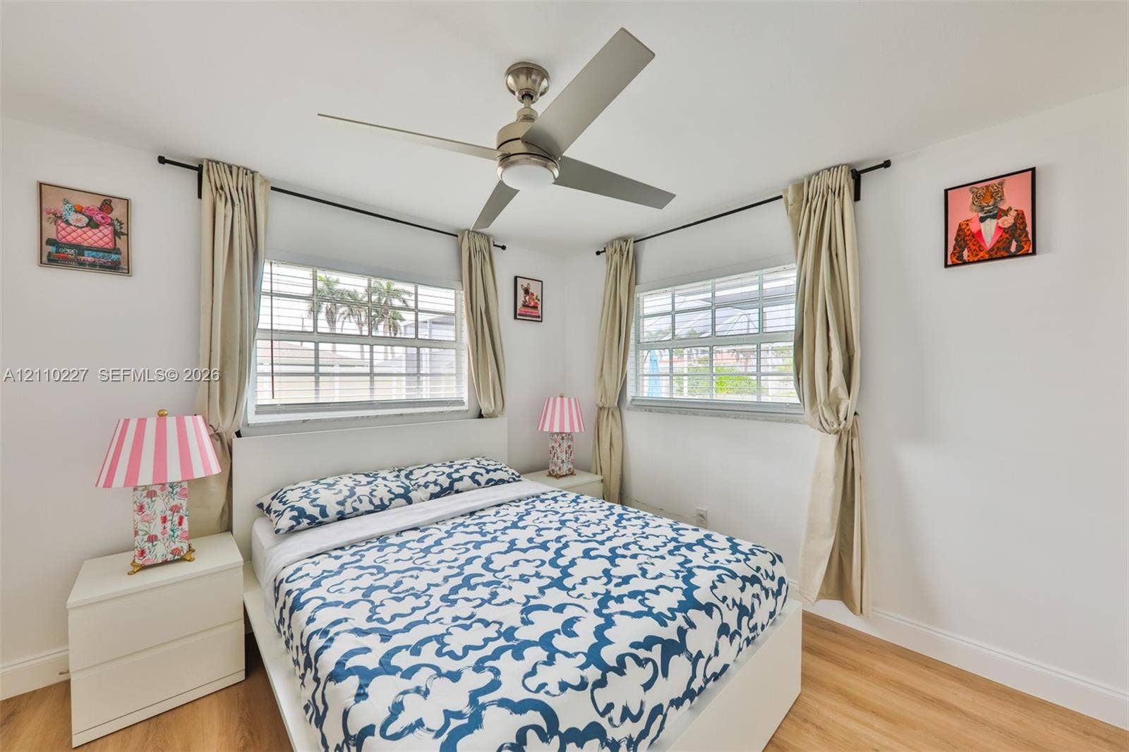 450 Bayshore Drive, Cape Coral, FL 33904 Neutral-toned interior featuring wood-finish flooring, dual windows with grid detailing, and a brushed-nickel ceiling fan with integrated lighting