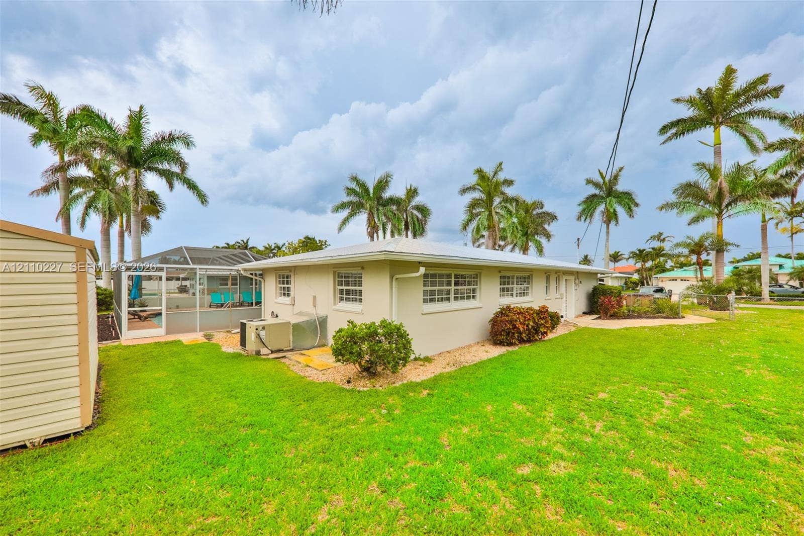 450 Bayshore Drive, Cape Coral, FL 33904 Exterior featuring a metal roof, screened-in enclosure, manicured lawn, established palm trees, and siding