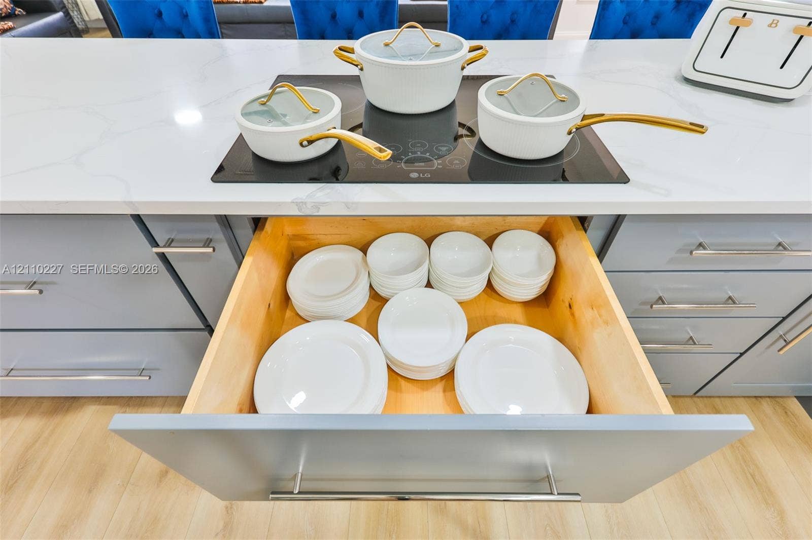 450 Bayshore Drive, Cape Coral, FL 33904 Kitchen island featuring a stone countertop with a flush-mounted induction cooktop, light-toned wood-finish flooring, and cabinetry with integrated pull-out drawer storage