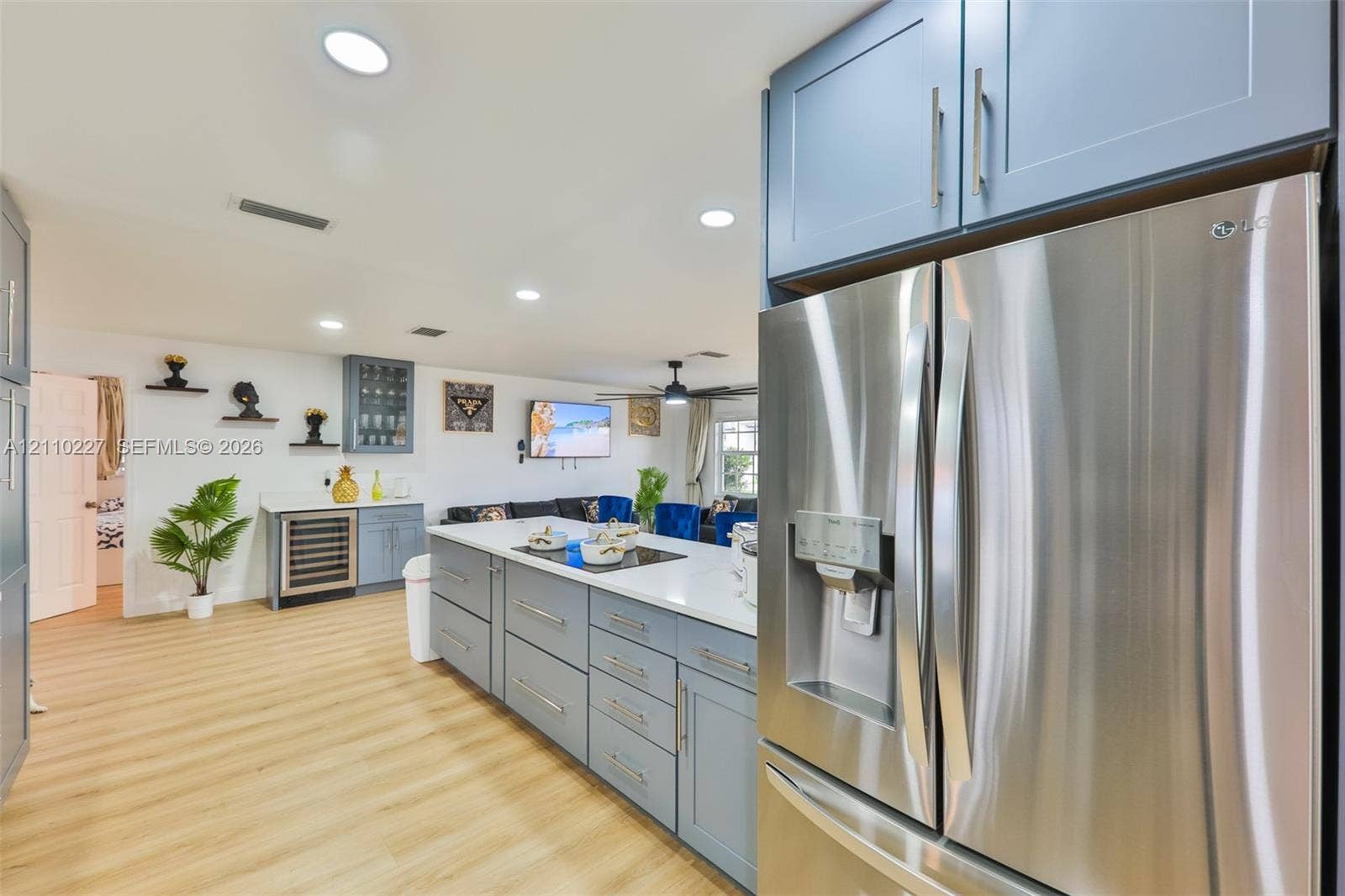 450 Bayshore Drive, Cape Coral, FL 33904 Kitchen featuring stainless steel refrigerator, large central island with light-toned countertop, built-in beverage cooler, shaker-style cabinetry, and wood-finish flooring