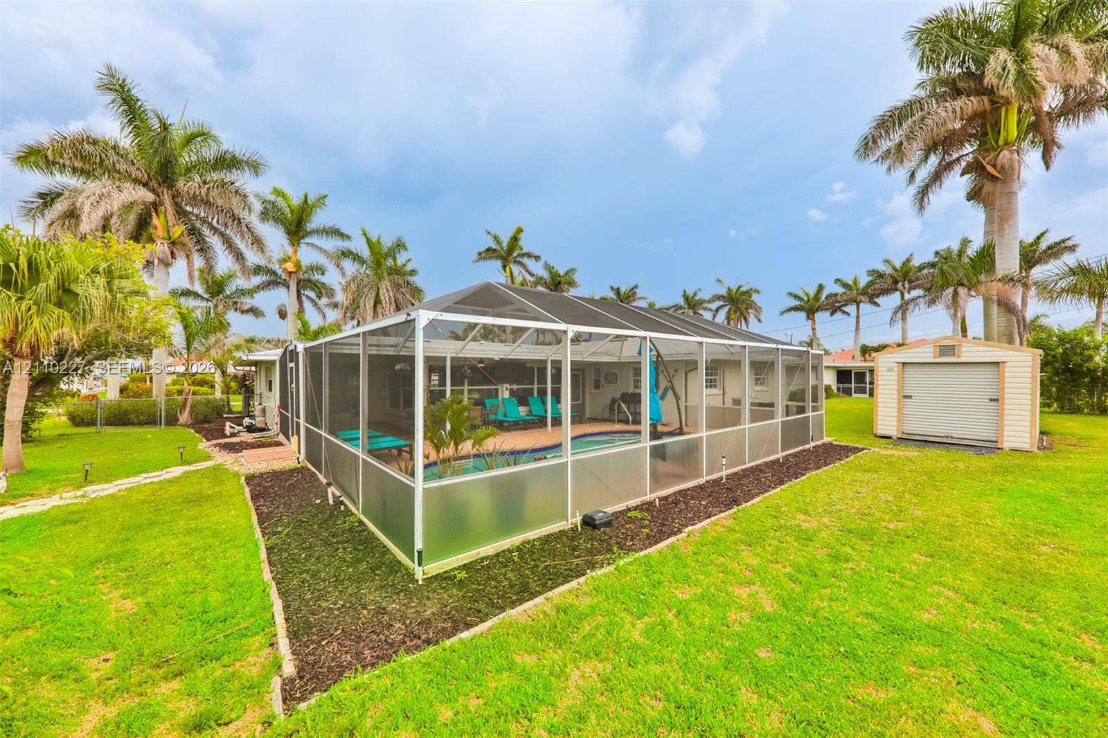 450 Bayshore Drive, Cape Coral, FL 33904 Screen-enclosed swimming pool featuring a paved deck and a detached storage shed situated on a lawn with mature palm trees