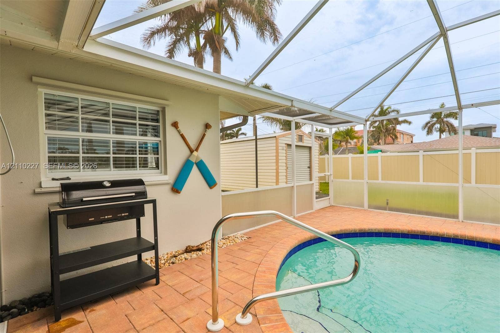 450 Bayshore Drive, Cape Coral, FL 33904 Screened-in enclosure featuring a private pool with a paved deck, perimeter privacy fencing, and exterior storage structure