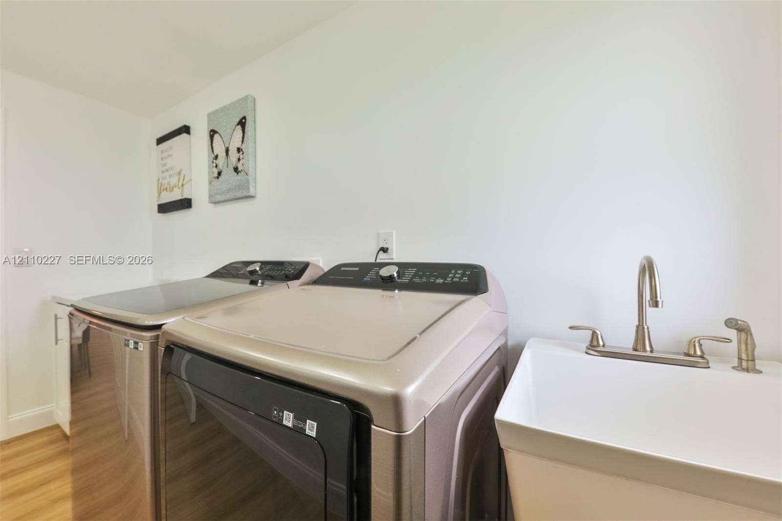 450 Bayshore Drive, Cape Coral, FL 33904 Laundry area featuring a drop-in utility sink with a high-arch faucet, side-by-side washer and dryer, white cabinetry, and wood-finish flooring