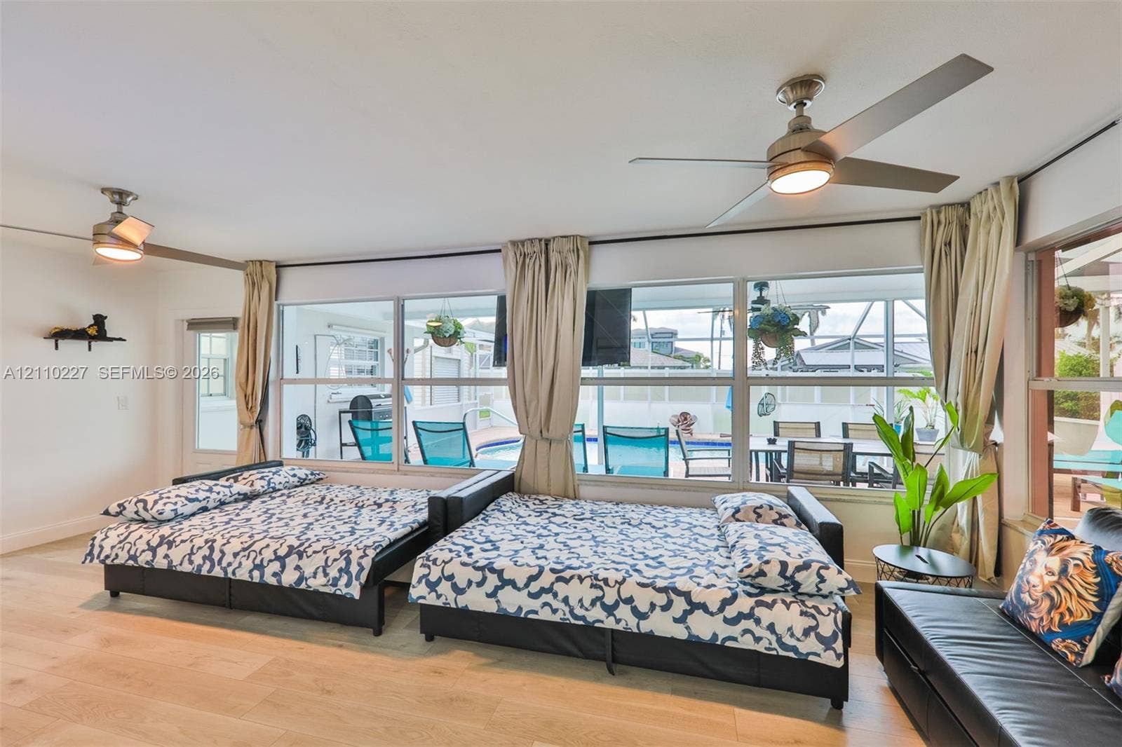 450 Bayshore Drive, Cape Coral, FL 33904 Spacious room featuring wood-finish flooring, two ceiling fans with integrated lighting, and a wall of floor-to-ceiling windows