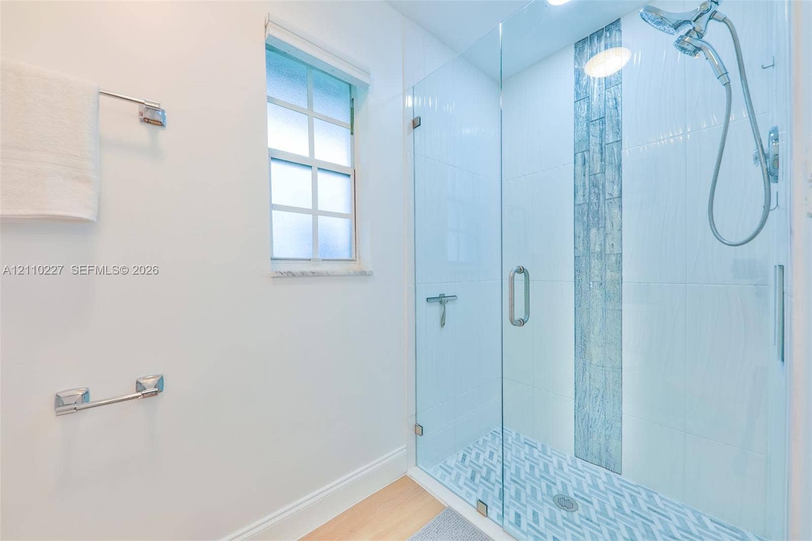 450 Bayshore Drive, Cape Coral, FL 33904 Walk-in shower featuring a glass enclosure, vertical decorative tile inlay, patterned tile flooring, and a multi-function showerhead