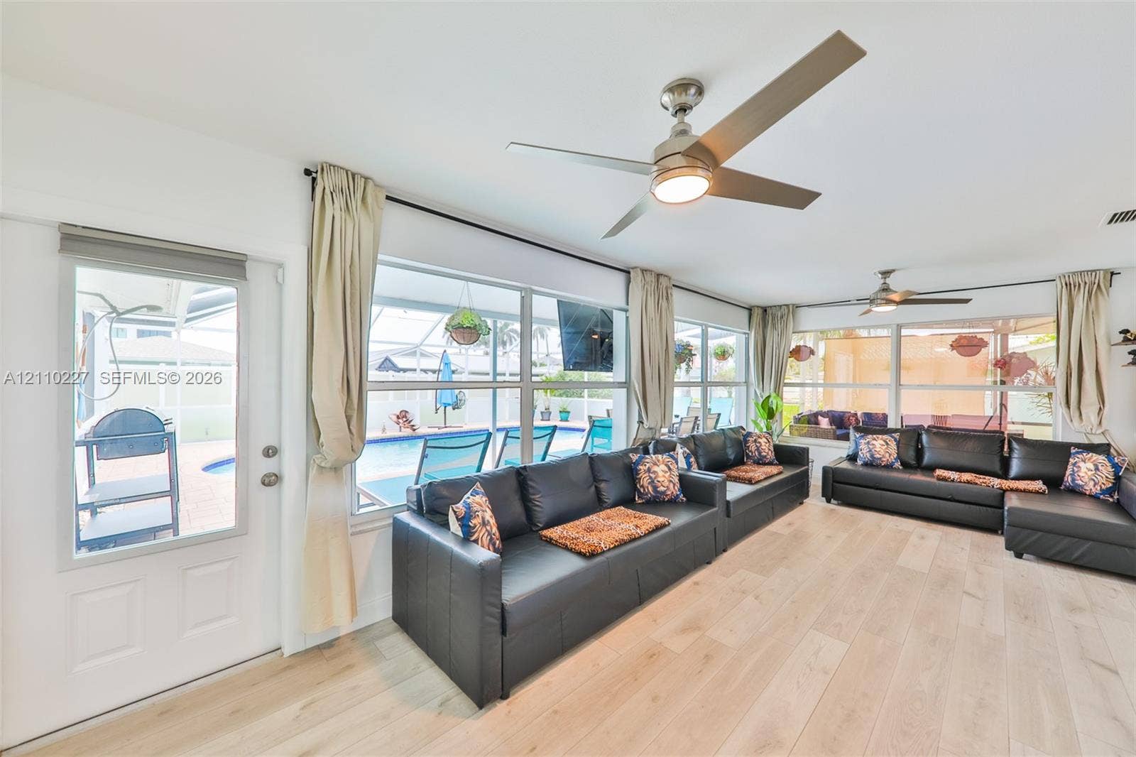 450 Bayshore Drive, Cape Coral, FL 33904 Light-filled sunroom featuring wood-finish flooring, dual ceiling fans, expansive windows, and a glass-paneled entry door