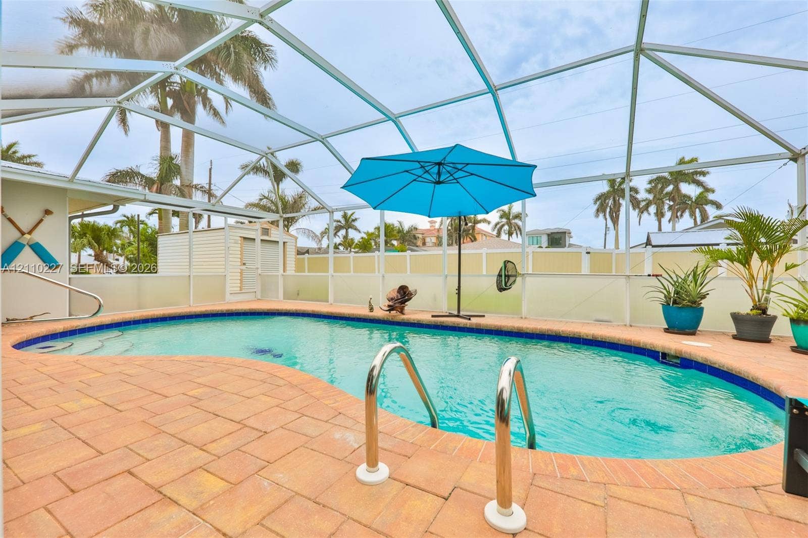 450 Bayshore Drive, Cape Coral, FL 33904 Screened-in pool area featuring paver decking, curved pool architecture with built-in stairs, metal handrails, and a detached storage structure
