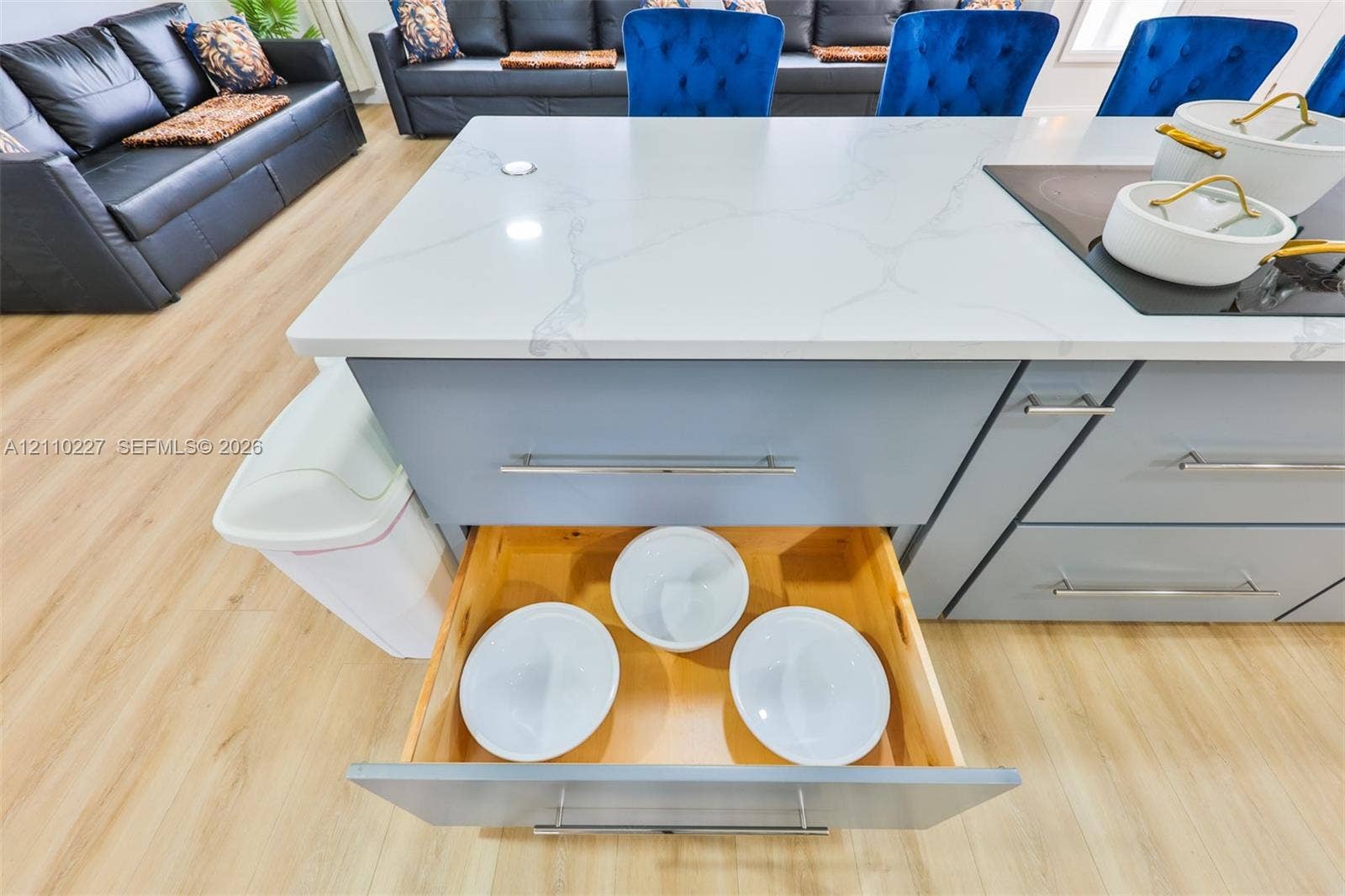 450 Bayshore Drive, Cape Coral, FL 33904 Center island featuring a stone-look countertop, integrated electric cooktop, light blue cabinetry with brushed metal hardware, and soft-close pull-out drawers with natural wood interiors, finished with wood-tone flooring