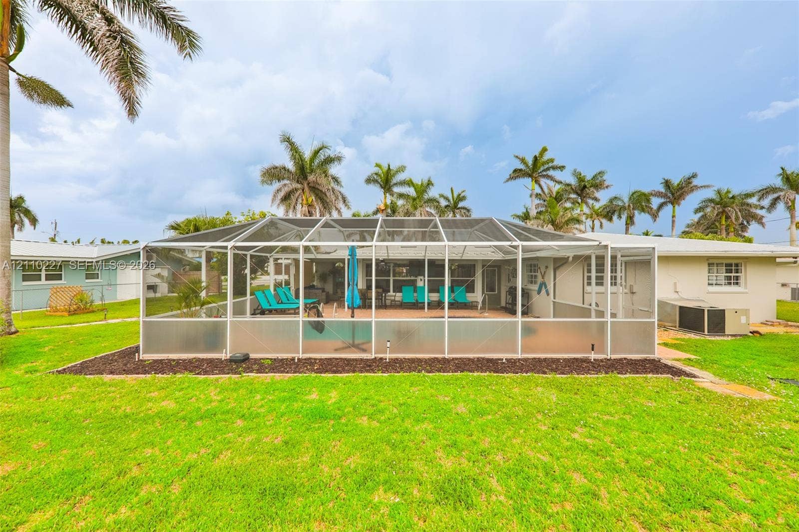 450 Bayshore Drive, Cape Coral, FL 33904 Screen-enclosed swimming pool featuring a paved deck, surrounded by a manicured lawn with mature palm trees