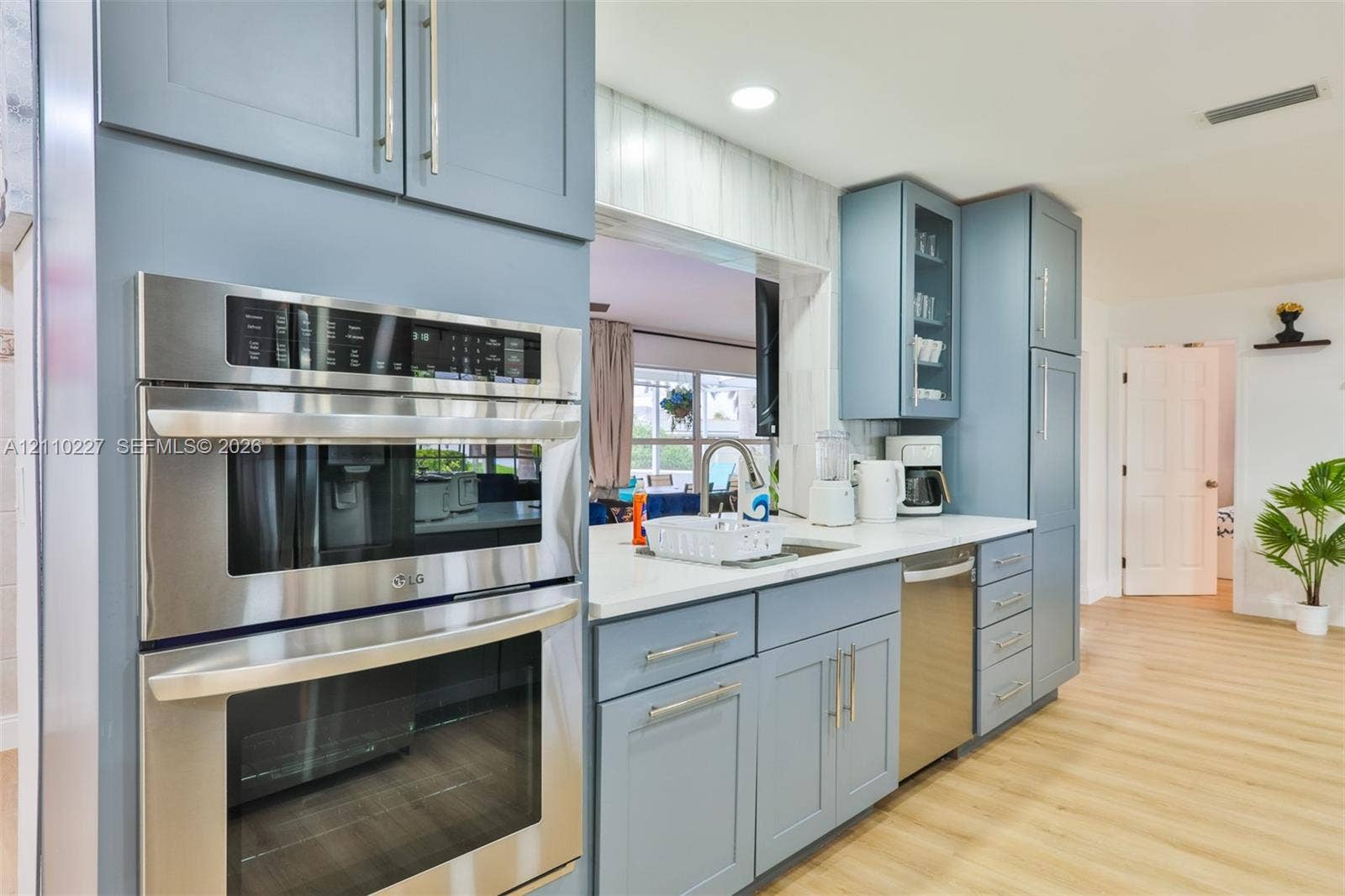 450 Bayshore Drive, Cape Coral, FL 33904 Kitchen featuring blue cabinetry, light-toned countertops, a built-in stainless steel double wall oven, a stainless steel dishwasher, and wood-finish flooring