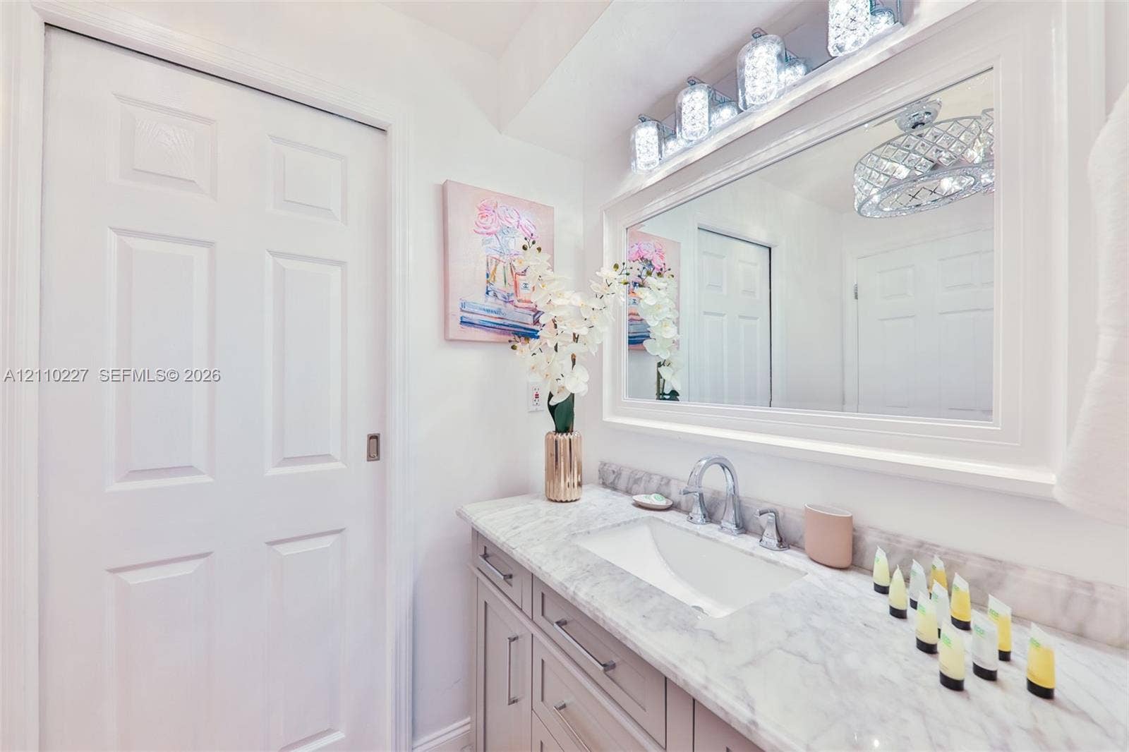 450 Bayshore Drive, Cape Coral, FL 33904 Vanity featuring a stone-look countertop with an integrated rectangular basin, contemporary metallic faucet, recessed cabinetry, and a large, framed mirror with integrated multi-bulb lighting