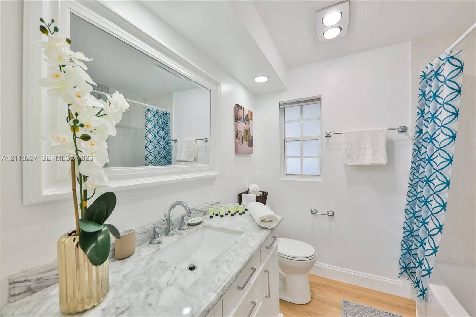 450 Bayshore Drive, Cape Coral, FL 33904 Bathroom featuring a stone-top vanity with an undermount sink, framed wall-to-wall mirror, wood-finish flooring, recessed ceiling lighting, and a multi-pane window
