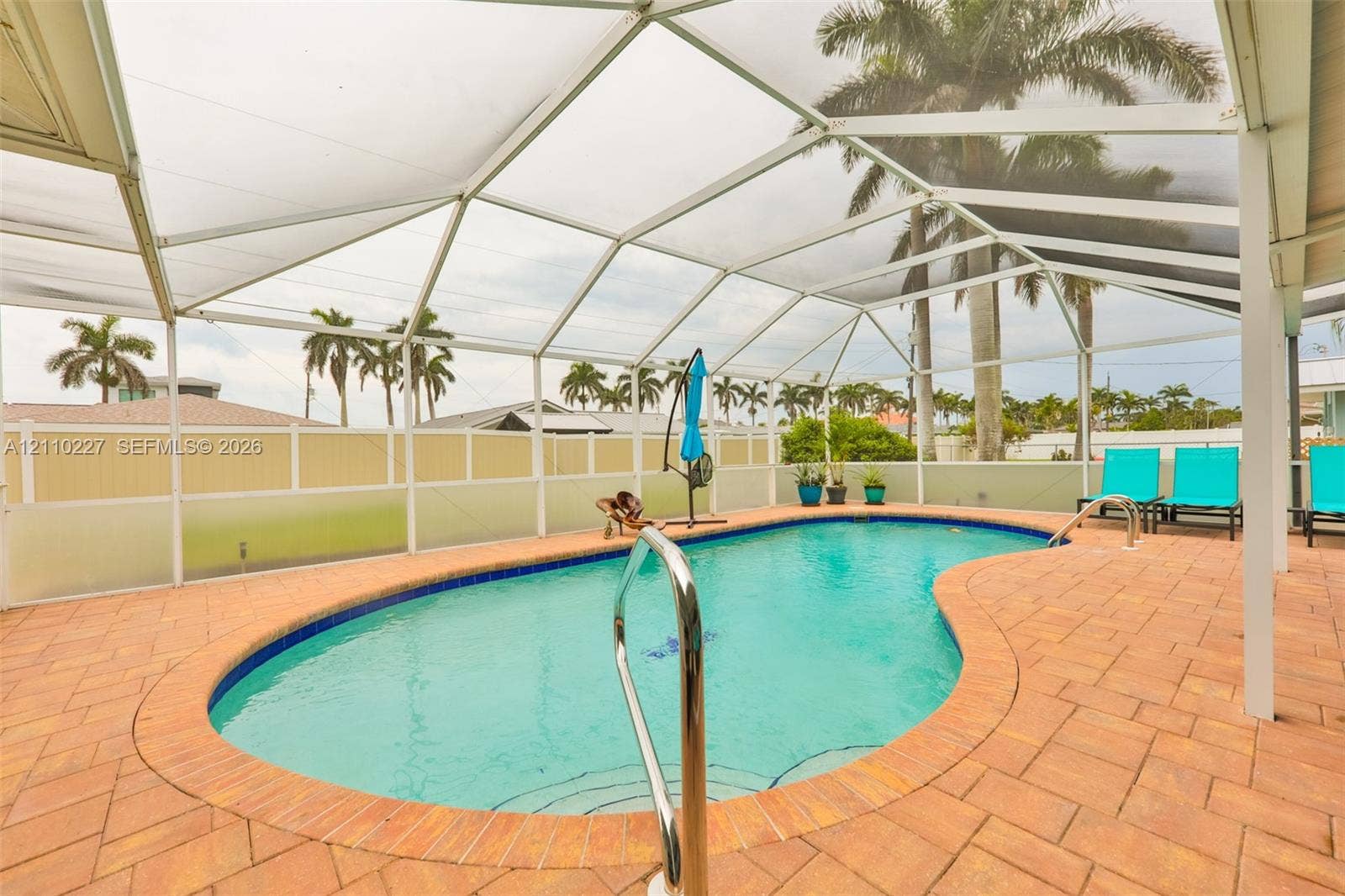 450 Bayshore Drive, Cape Coral, FL 33904 Screened-in patio featuring a kidney-shaped swimming pool, brick paver decking, and a metal pool ladder