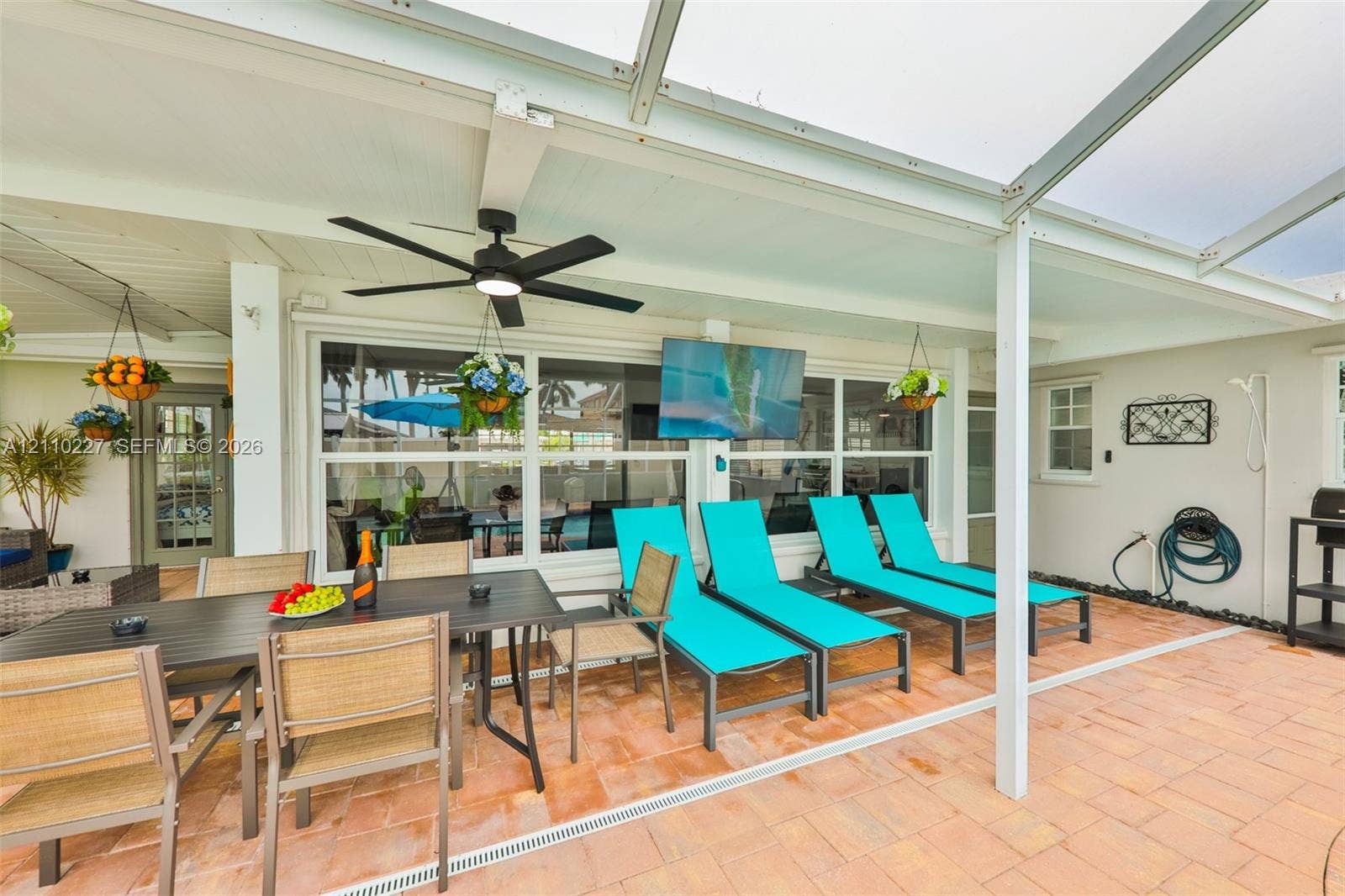 450 Bayshore Drive, Cape Coral, FL 33904 Covered patio featuring paver flooring, a screened enclosure, a ceiling-mounted fan, and a wall-mounted television