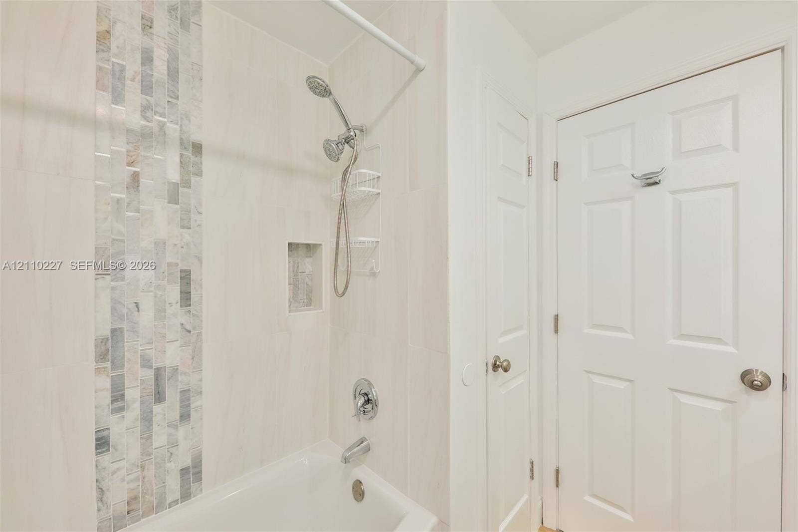 450 Bayshore Drive, Cape Coral, FL 33904 Bathtub and shower combination featuring large-format wall tile, a vertical decorative stone mosaic accent, an integrated wall niche, and polished chrome fixtures