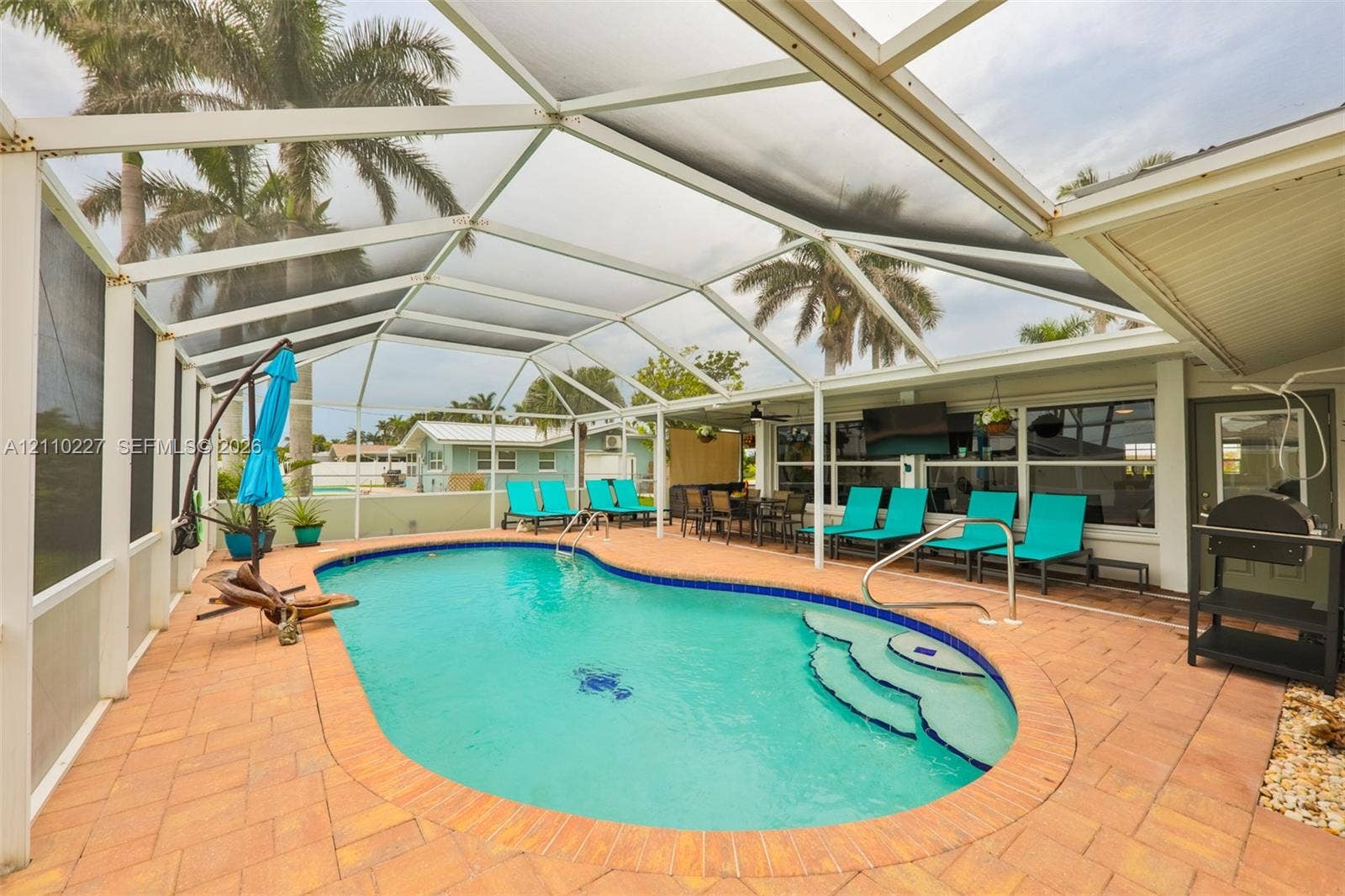 450 Bayshore Drive, Cape Coral, FL 33904 Screened-in patio featuring a kidney-shaped swimming pool, built-in steps, and expansive brick paver decking